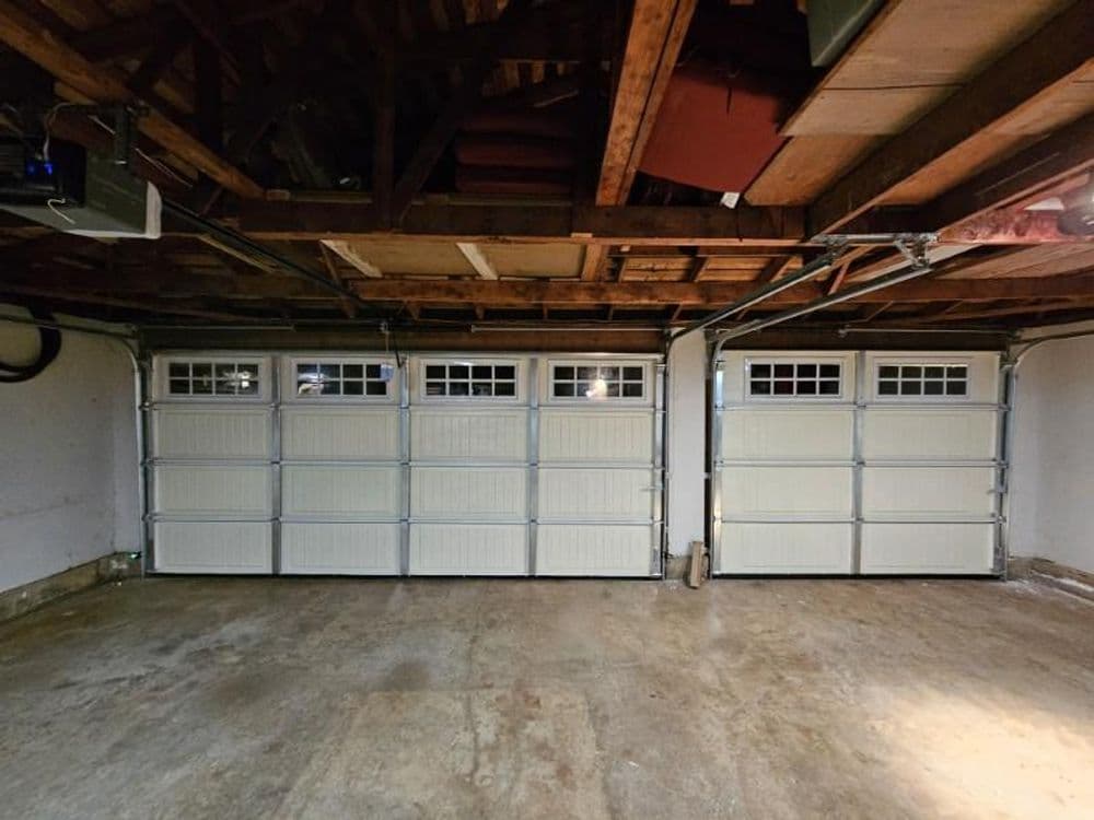 Interior view of a spacious garage with four white garage doors and a wooden ceiling.