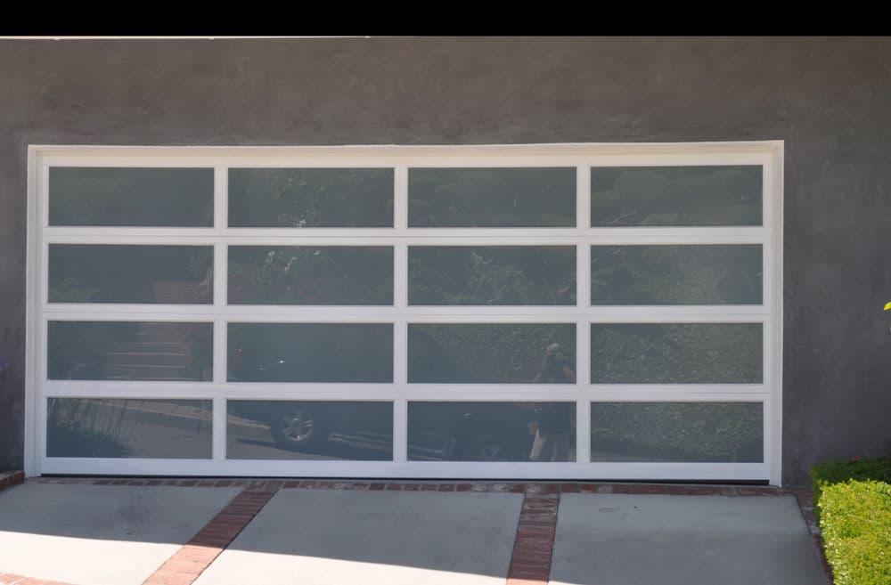 Modern garage door with glass panels and white frame, set against a gray wall.