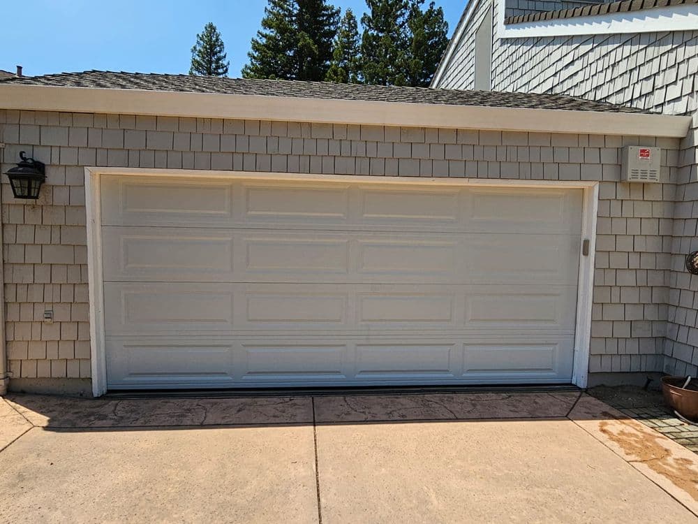 White garage door on a suburban home with textured siding and clear blue sky.