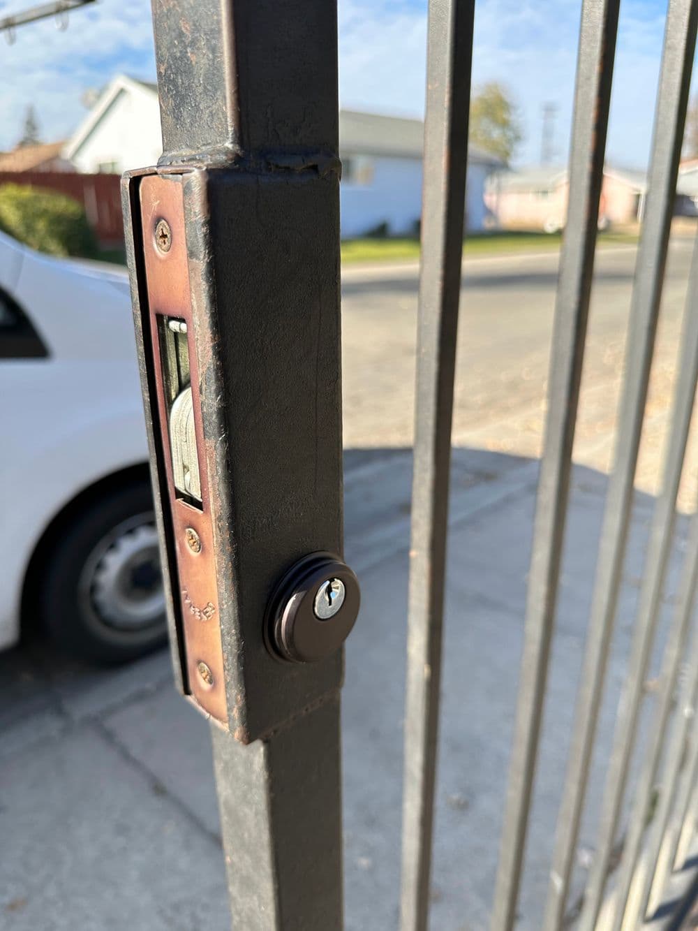Close-up of a gate lock with keyhole, featuring a secure sliding mechanism and residential background.