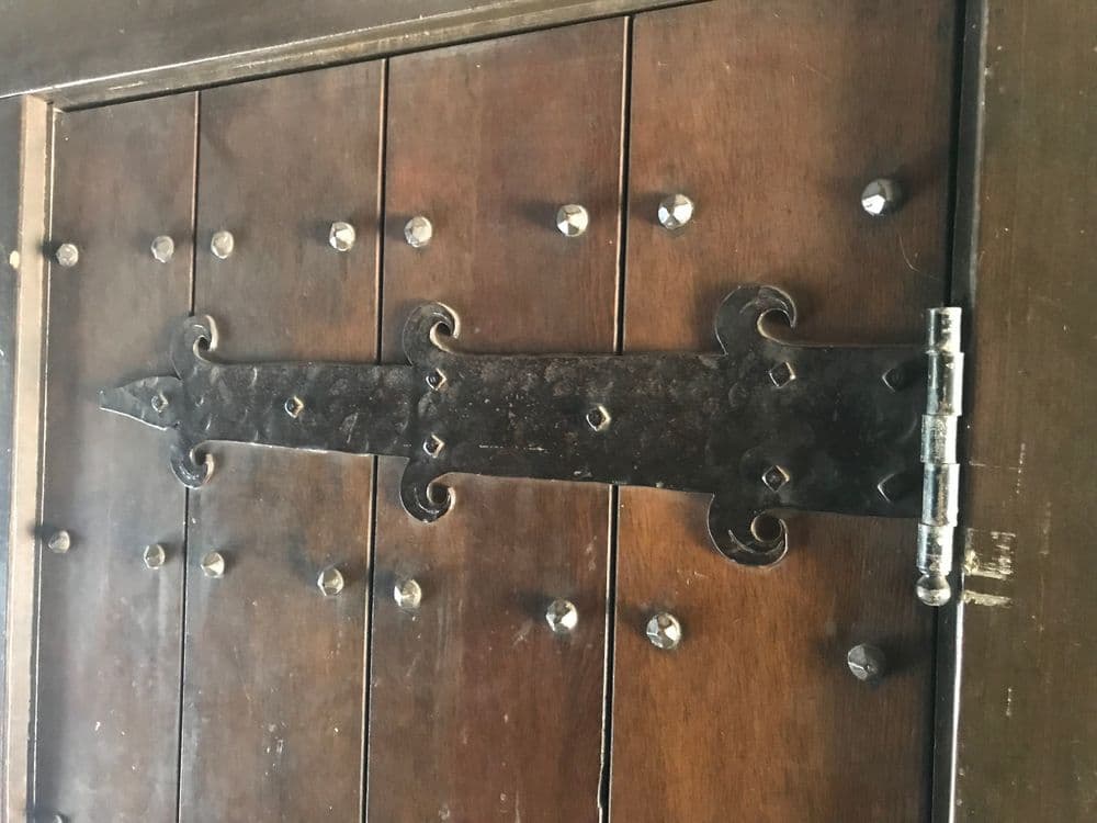 Rustic wooden door with metal hinge and decorative studs, showcasing vintage craftsmanship.