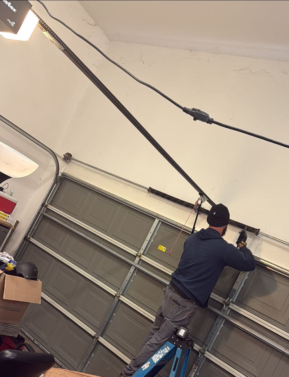 Person installing a garage door opener in a residential garage with tools and equipment.
