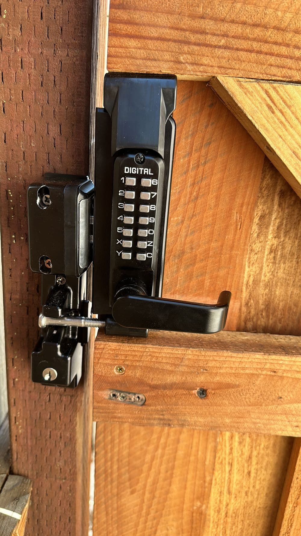 Digital lock on wooden gate with keypad and sleek black handle for secure access.