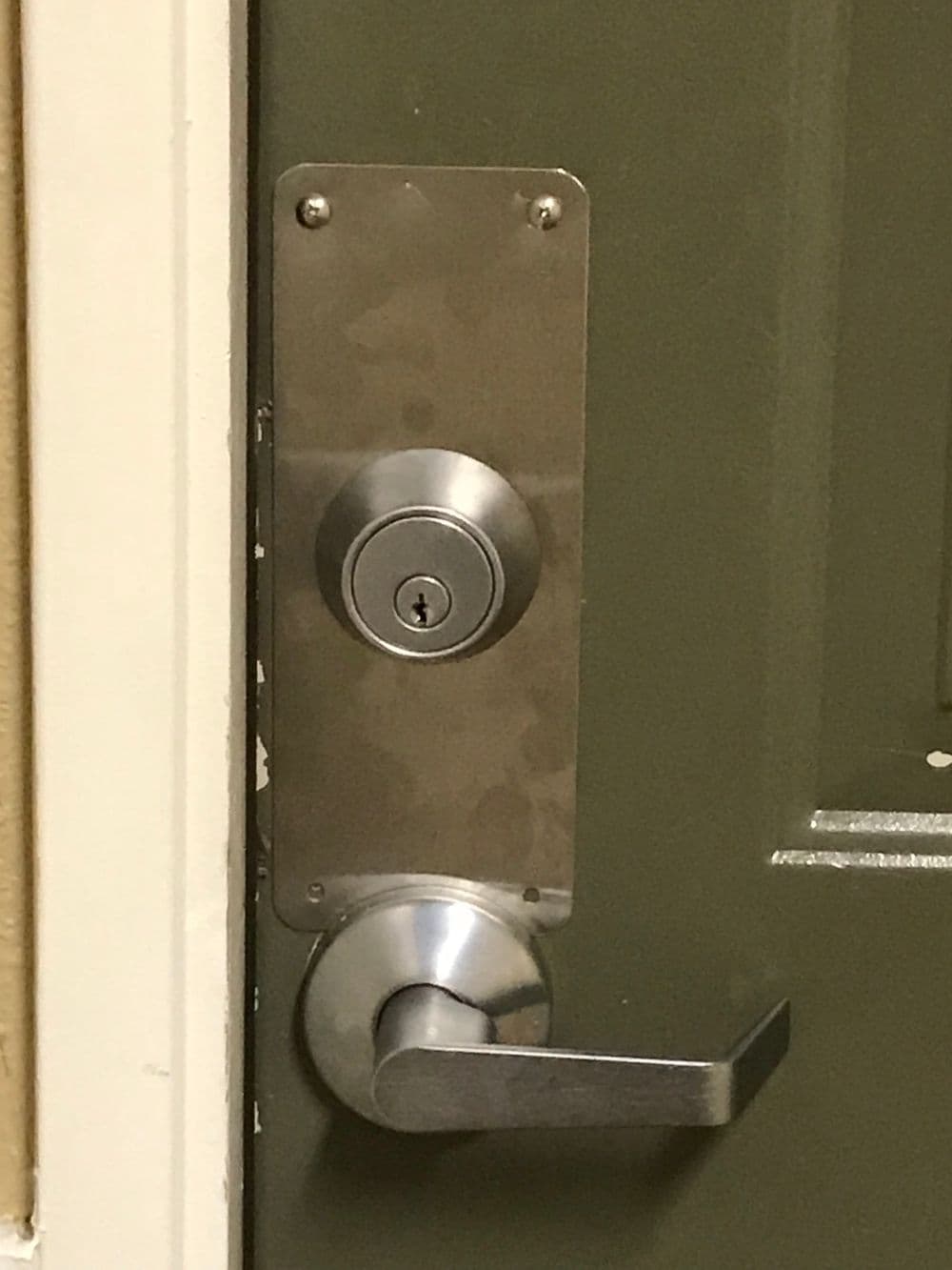 Close-up of a door lock and handle on a green door with a stainless steel plate.