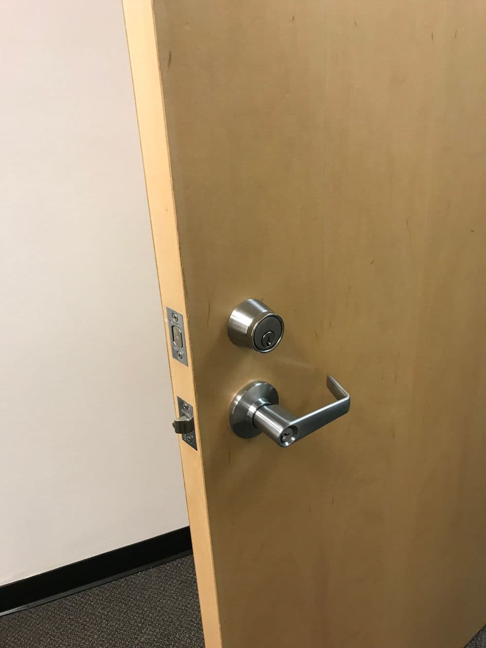 Wooden door partially open with a modern lock and lever handle.