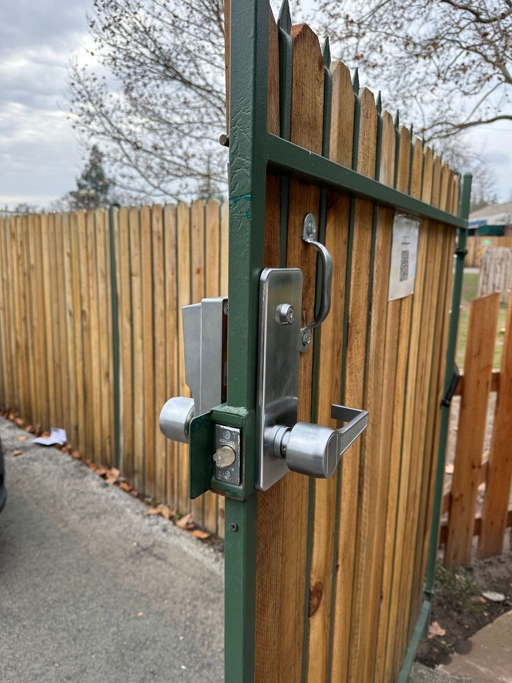 Close-up of a modern gate lock on a wooden fence with a green frame.