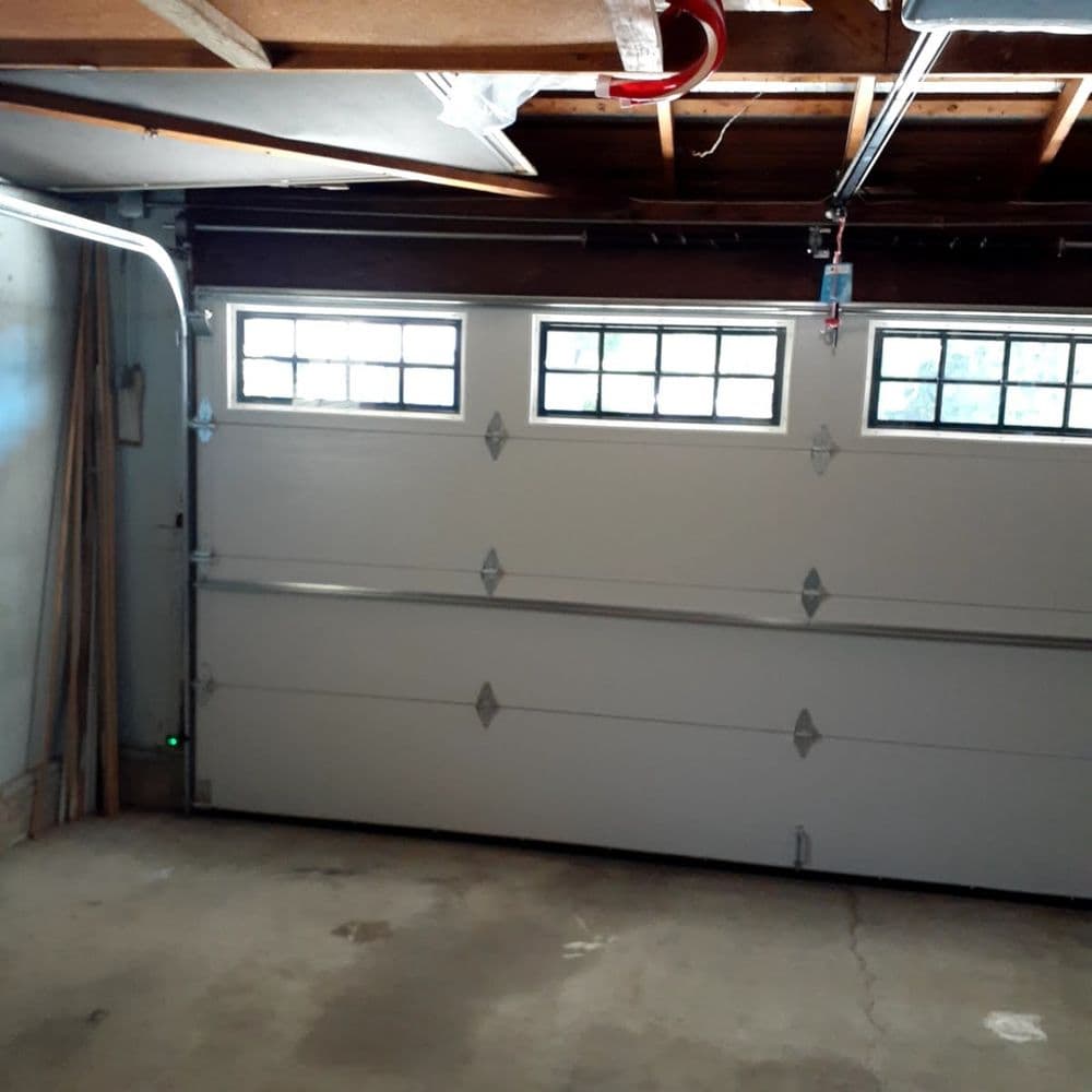 Interior of a garage featuring a closed white garage door with windows and wooden beams.