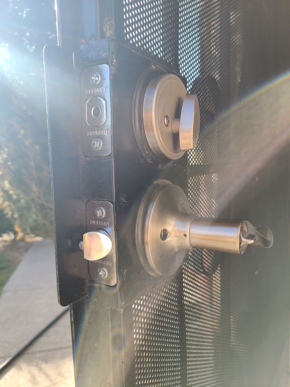 Close-up of a door lock with keyhole and keypad on a black security door. Sunlight highlighting details.