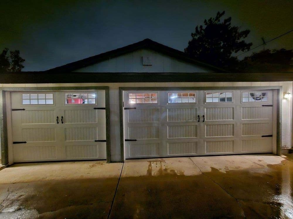 Three white garage doors with windows, illuminated at night in a residential setting.