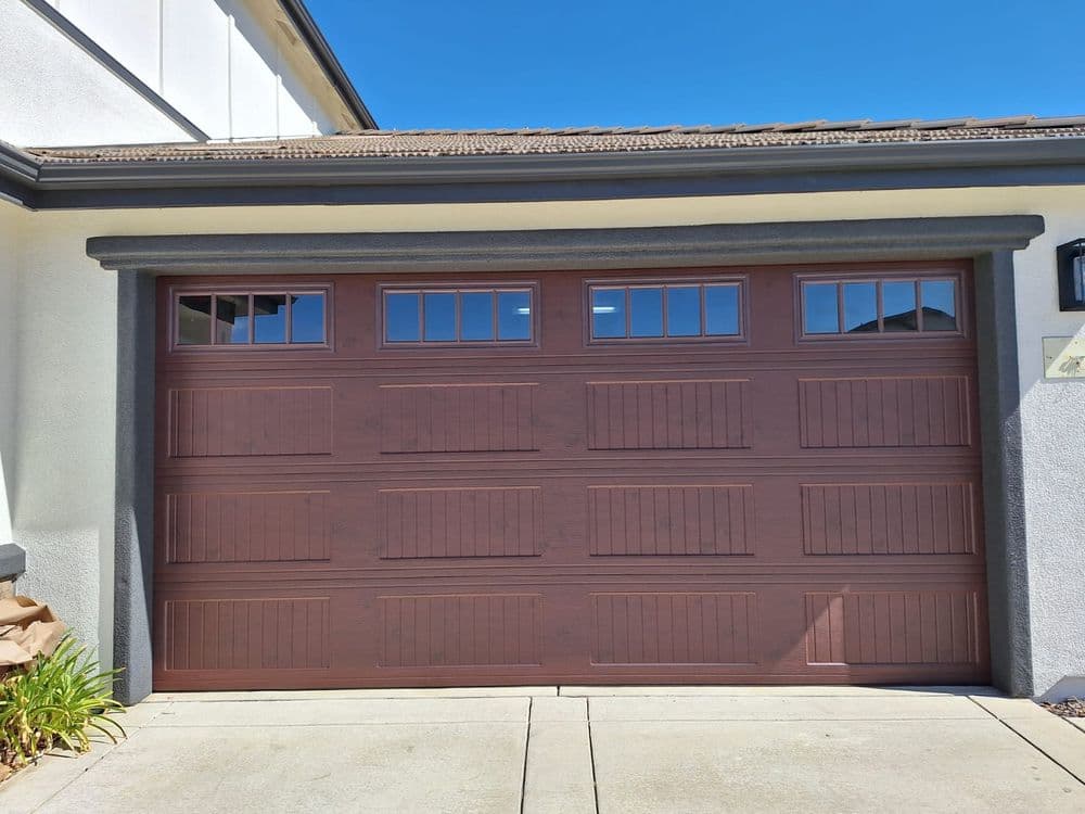 Modern brown garage door with window panels, featuring a textured design and clear blue sky.