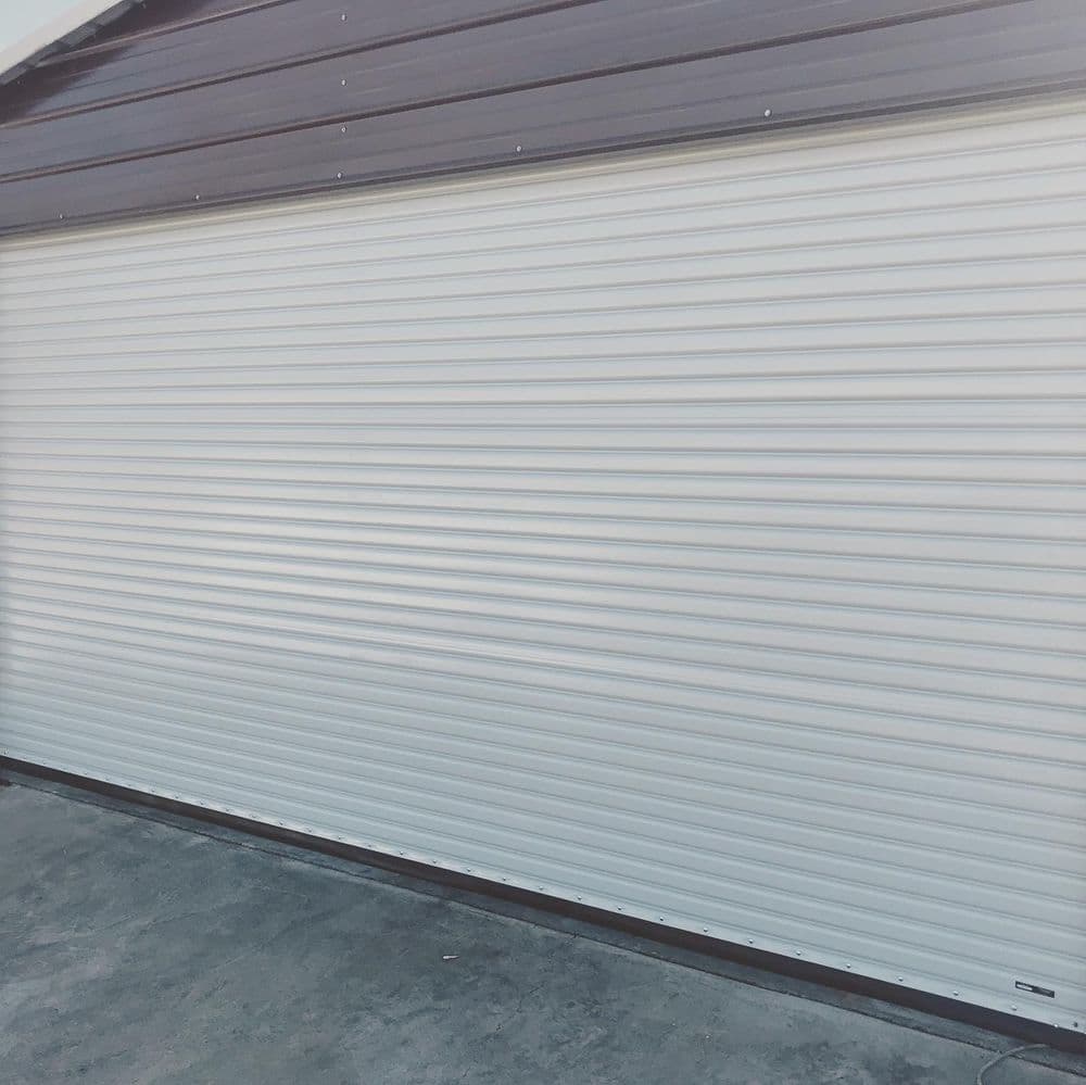 White rolling garage door on a brown building exterior. Ideal for security and convenience.