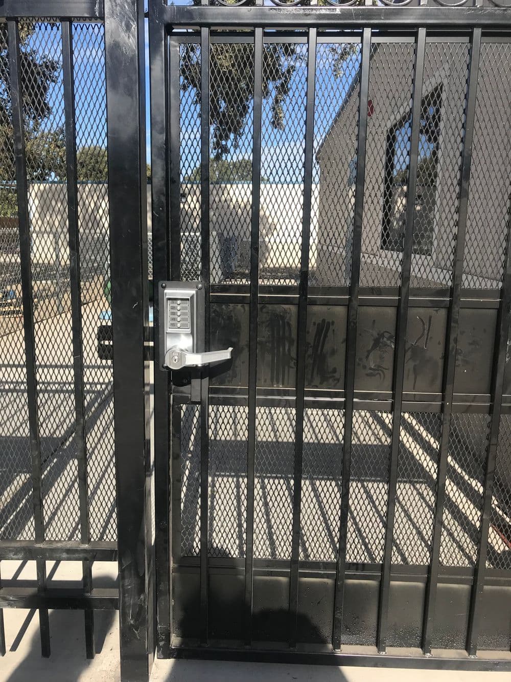Metal gate with mesh design and keypad lock, showcasing an entrance to a secured area.