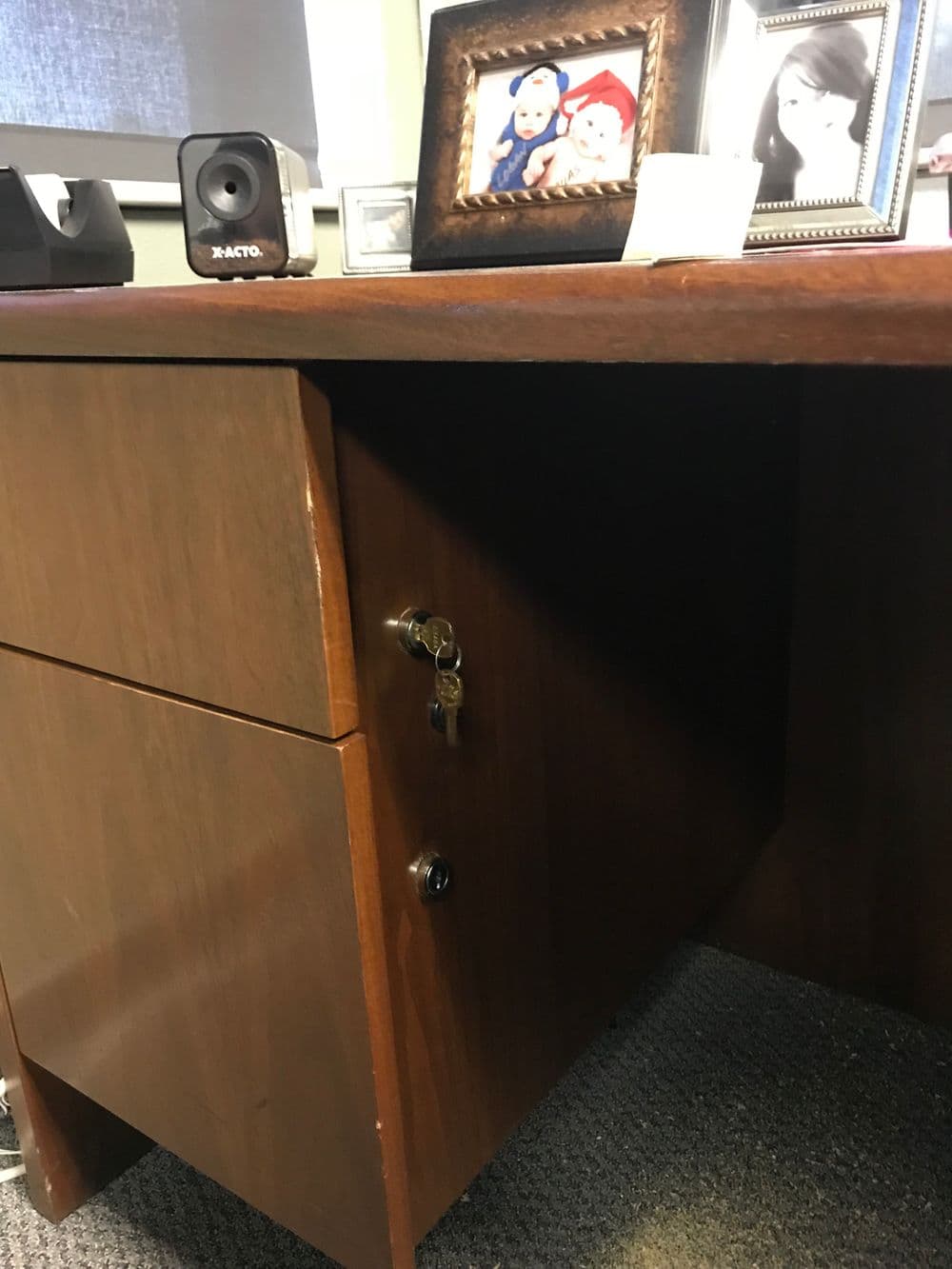 Wooden desk with a locked drawer, framed photos on top, and office supplies nearby.