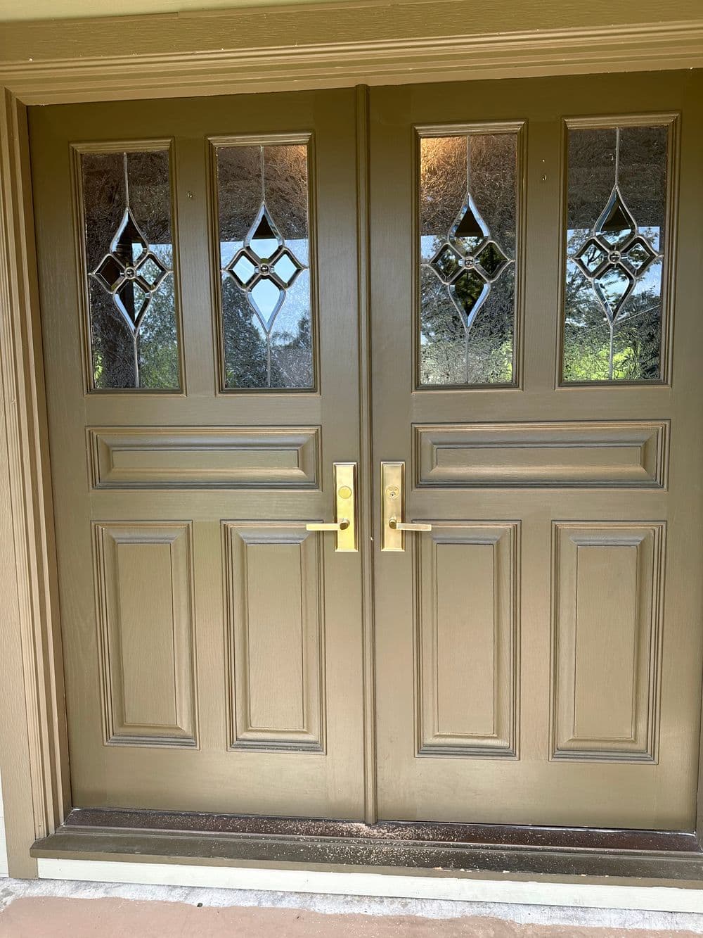 Elegant double front doors with decorative glass panels and polished gold handles.