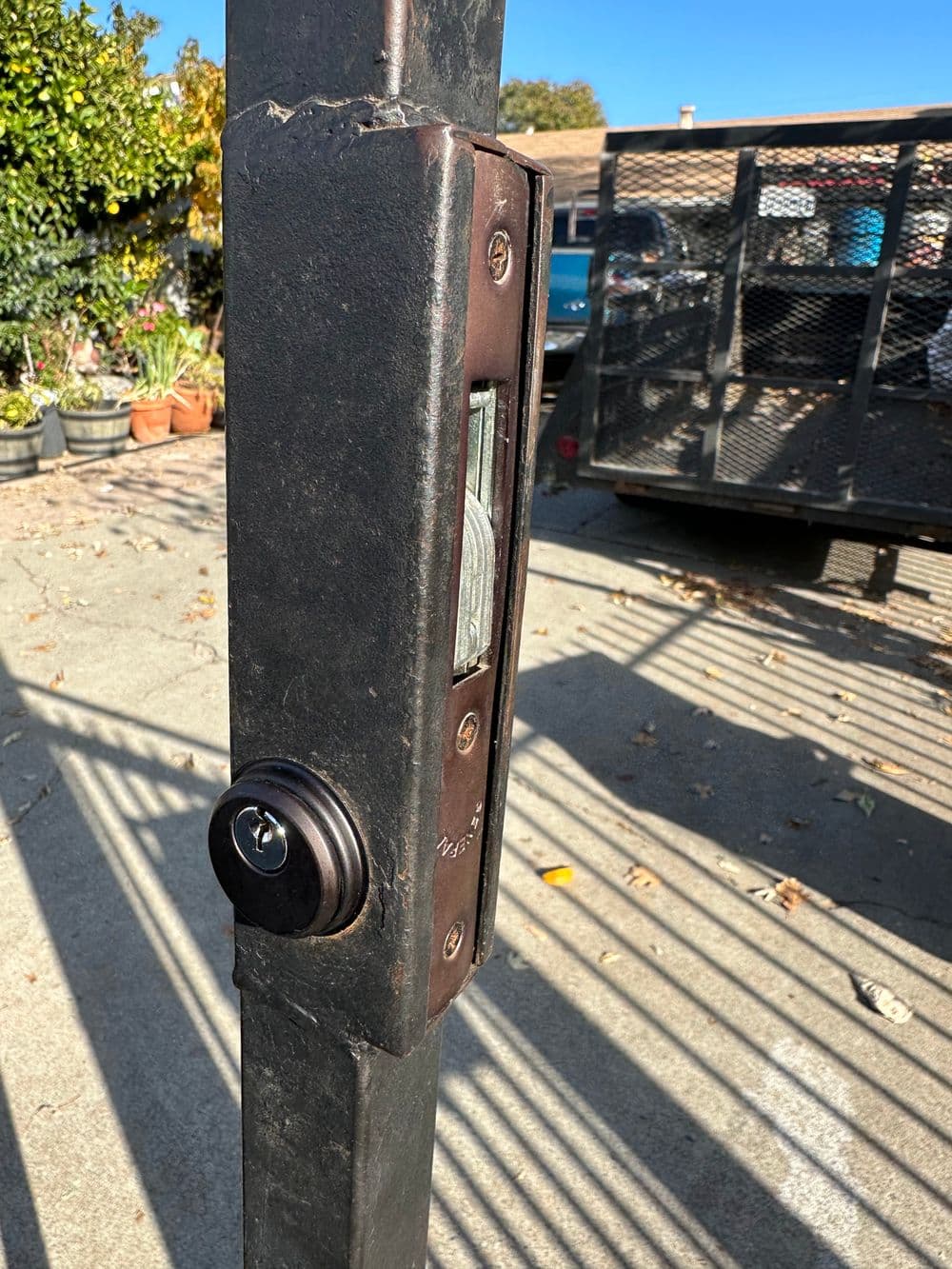 Close-up of a gate lock on a metal post in a sunny outdoor setting.