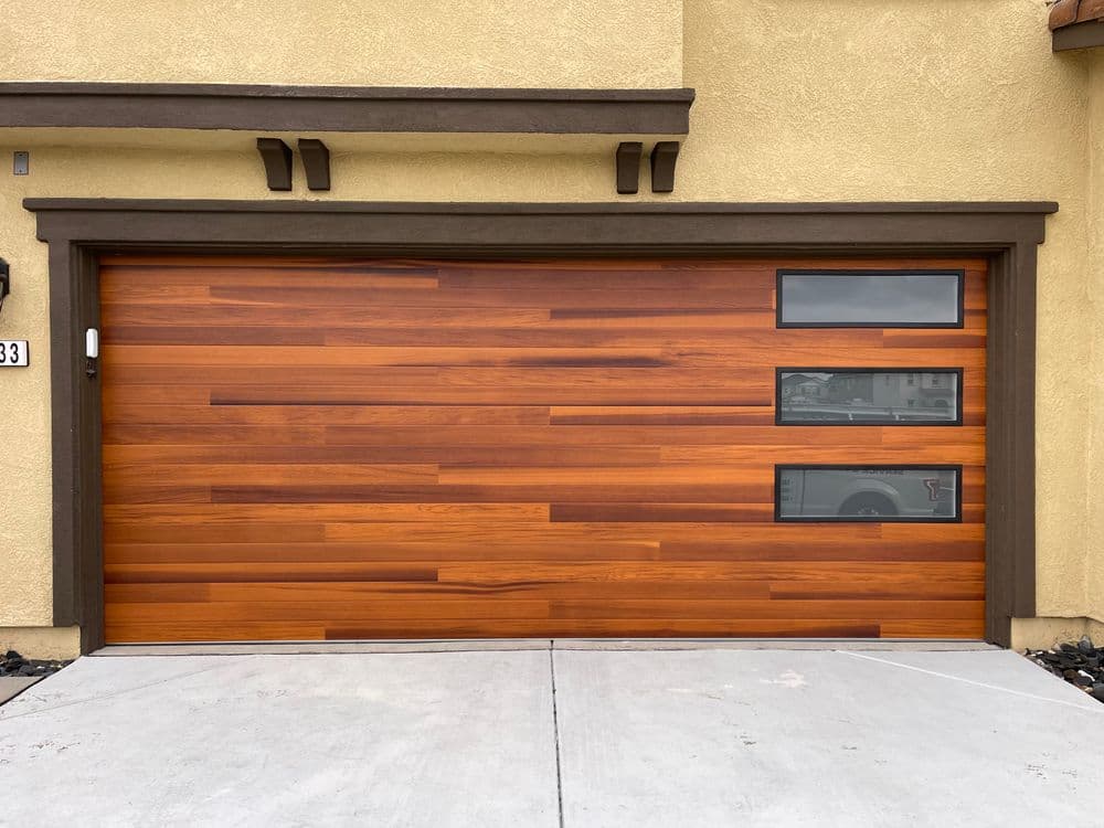 Modern wooden garage door with horizontal panels and large side windows, enhancing curb appeal.