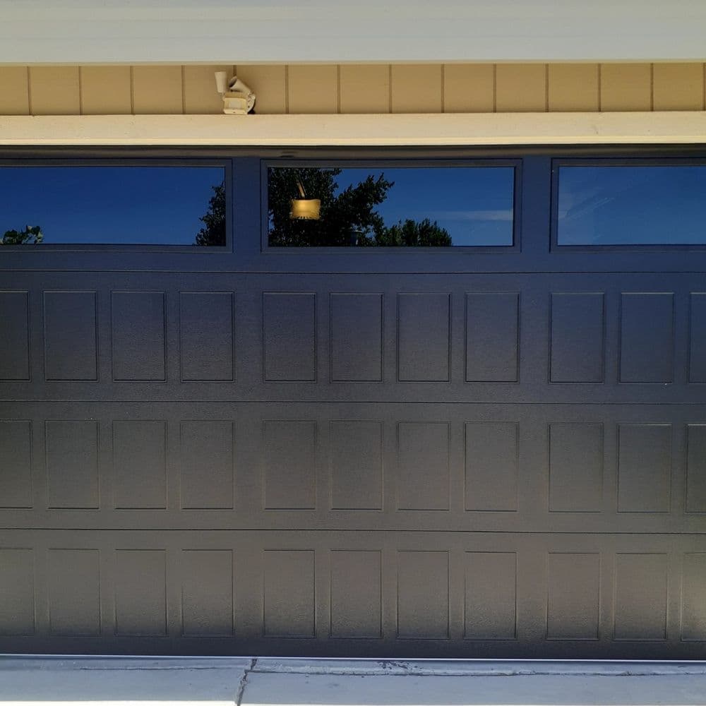 Black garage door with panel design and windows, set against a beige house exterior.