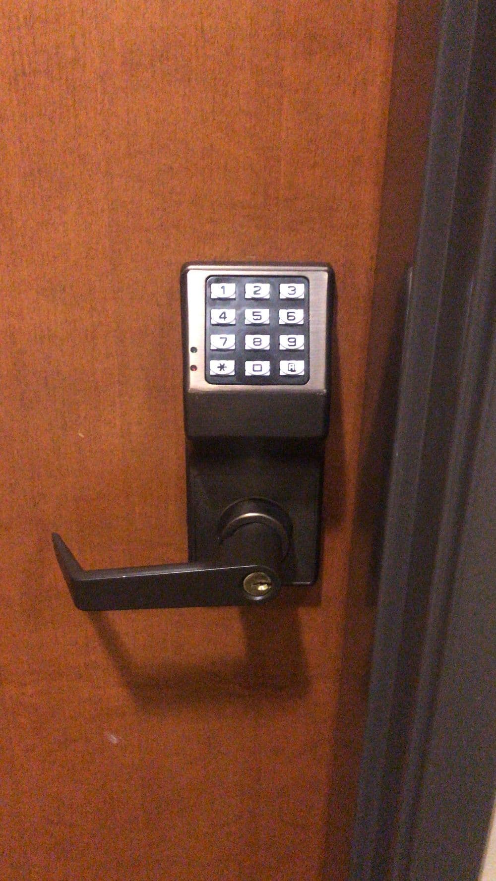 Electronic keypad lock on a wooden door with a lever handle for secure access.