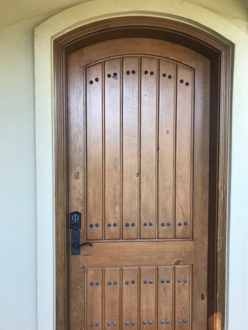Wooden arched door with vertical panels and decorative iron accents.