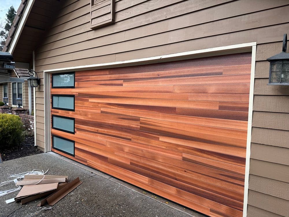 Modern wooden garage door with horizontal planks and glass panels on a suburban home.