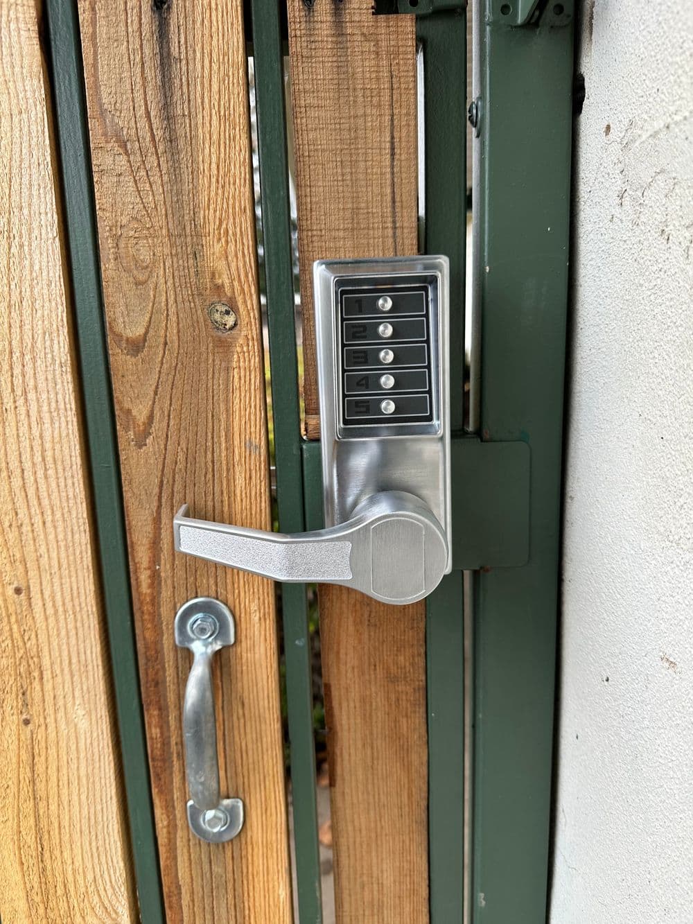 Digital keypad lock on a wooden gate, featuring a lever handle and five-digit entry panel.
