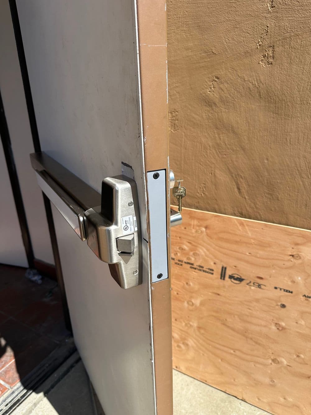 Exterior door with a secure locking mechanism and plywood board covering surrounding area.