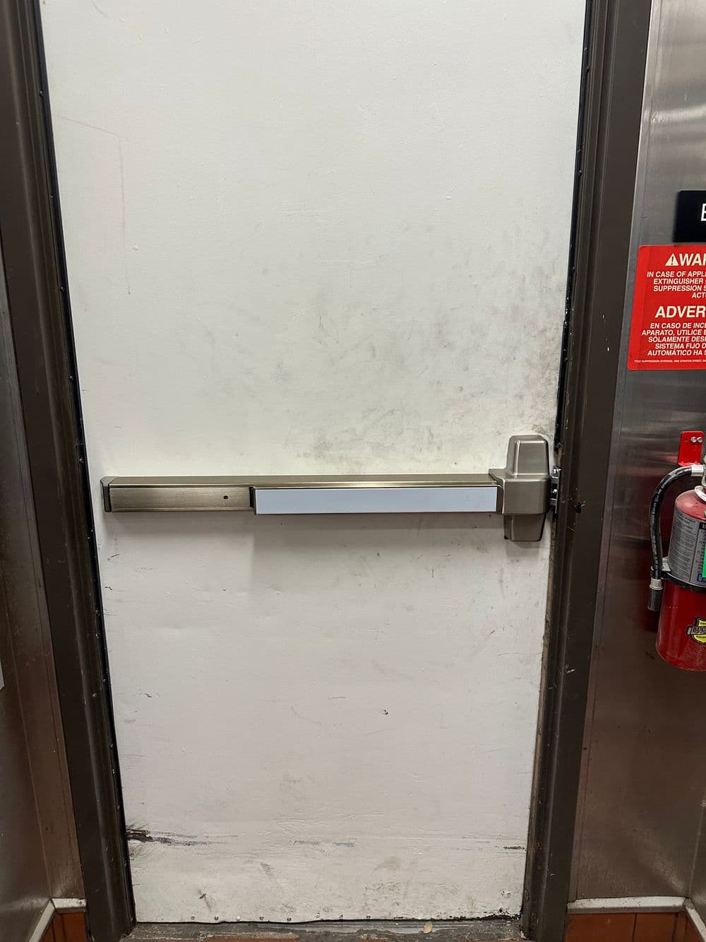 Panic exit door with horizontal bar handle and fire extinguisher nearby.