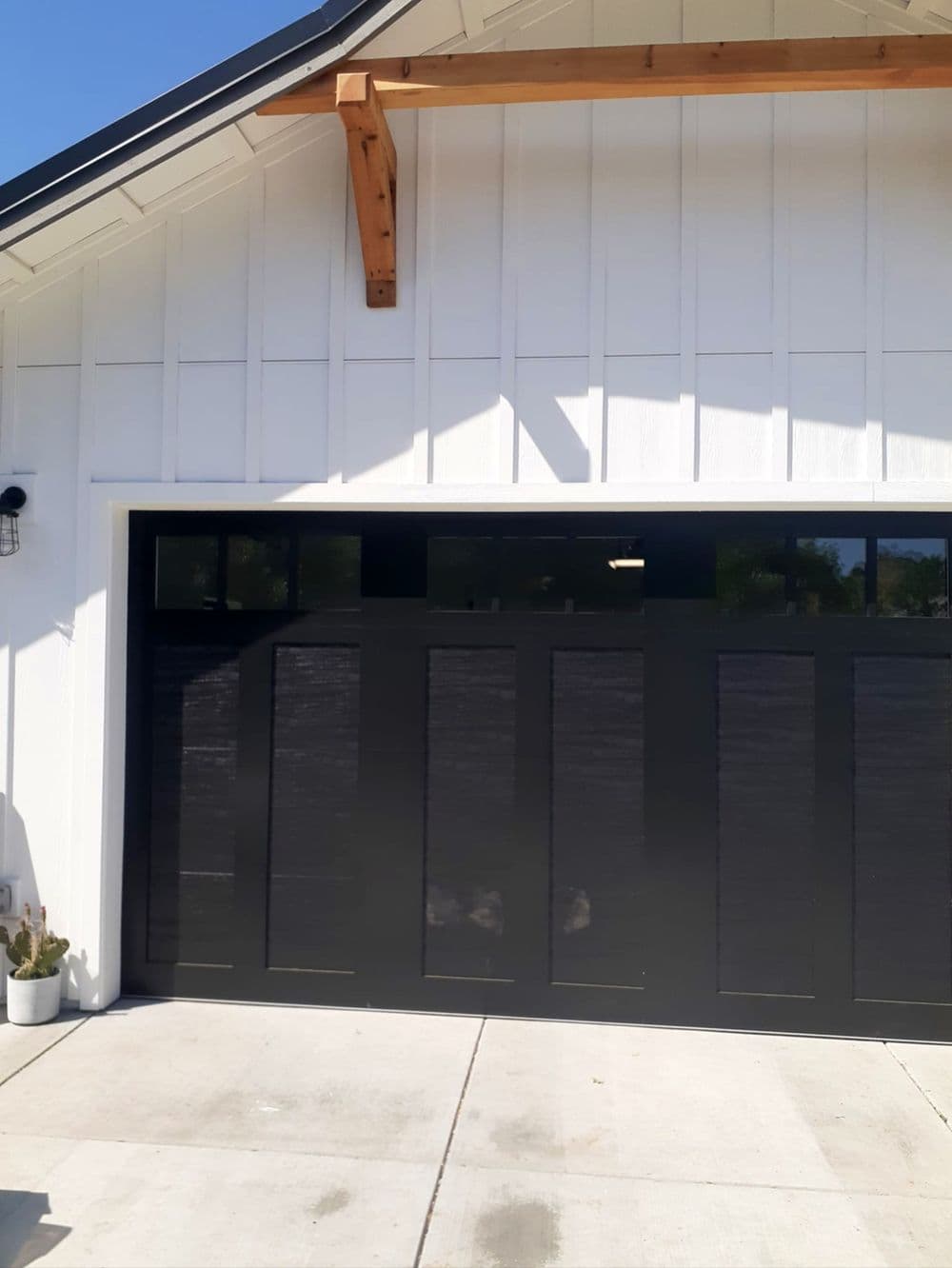 Modern black garage door on a white house exterior with wooden accents. Bright and clean design.