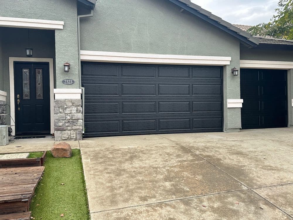 Modern home exterior with gray walls and two black garage doors on concrete driveway.