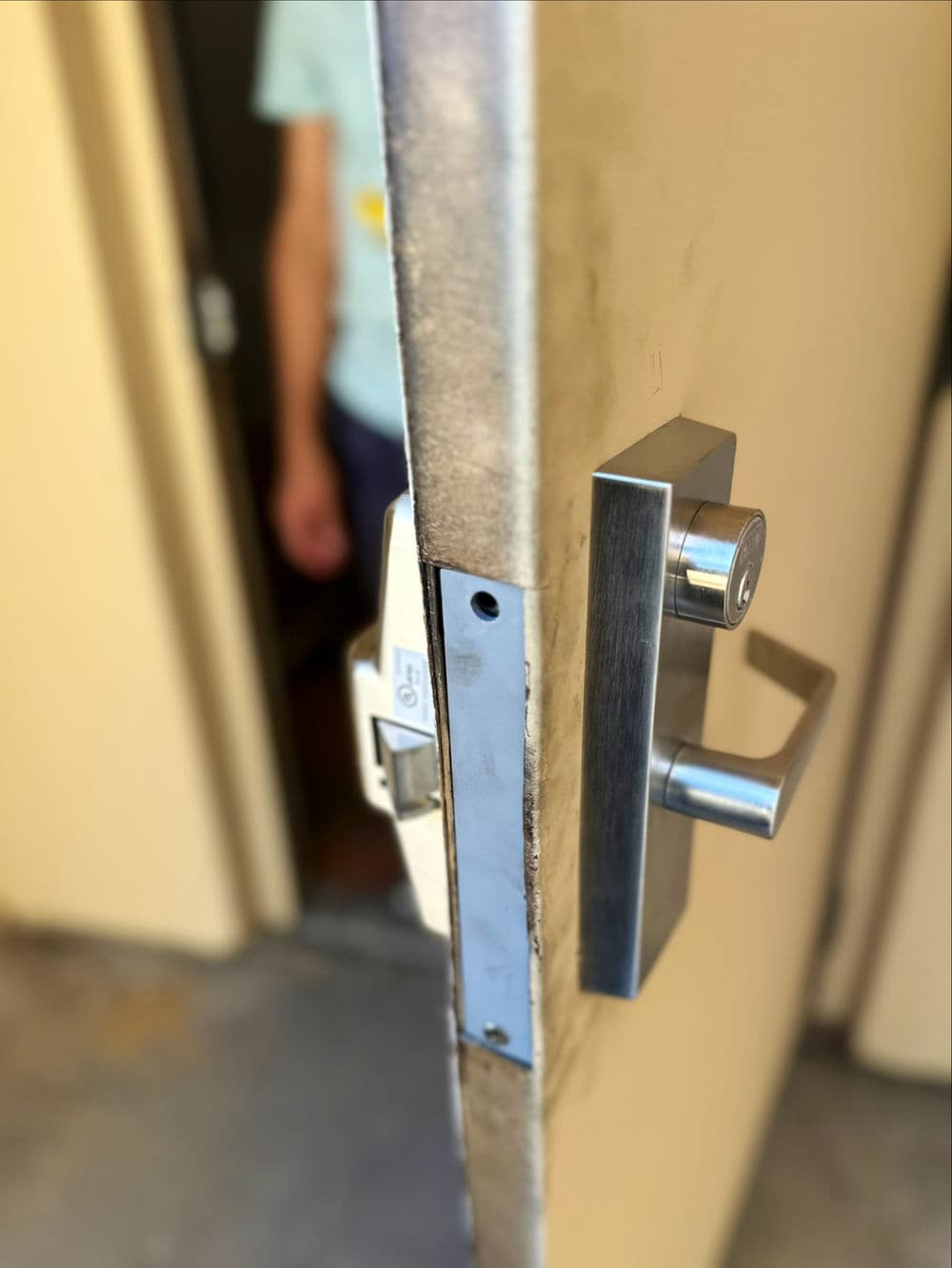 Close-up of a modern door handle and lock with a blurred figure in the background.