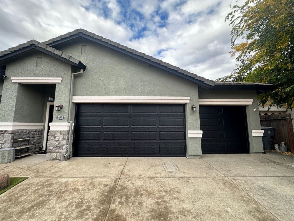 Modern home exterior with dual black garage doors and stone accents under a cloudy sky.