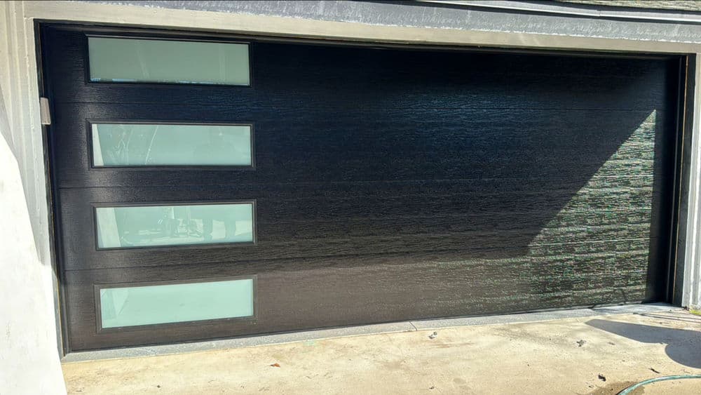 Modern black garage door with three rectangular glass windows. Stylish and contemporary design.