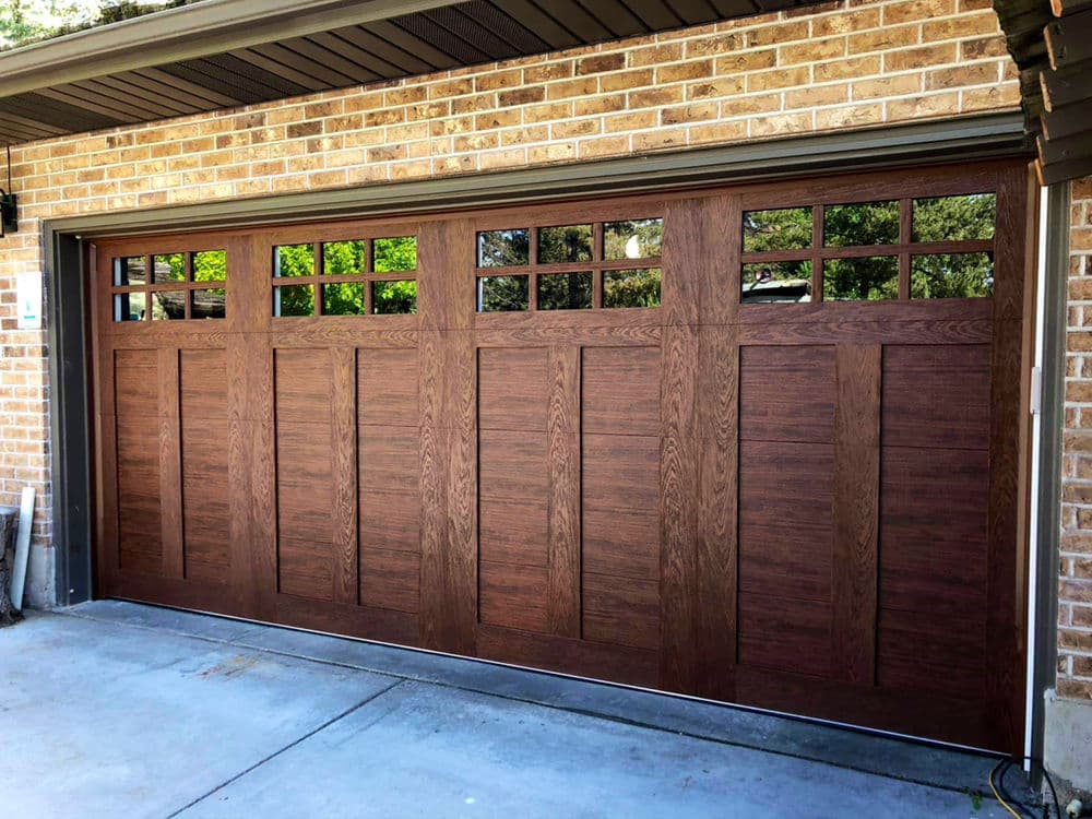 Brown wooden garage door with decorative windows on a brick wall. Modern design for homes.
