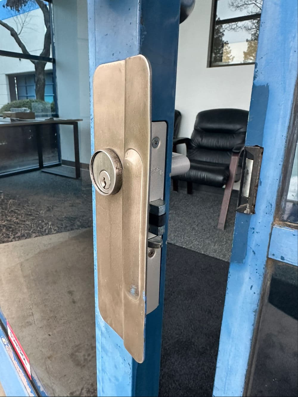 Brass door lock on blue entrance door with leather chairs in the background.