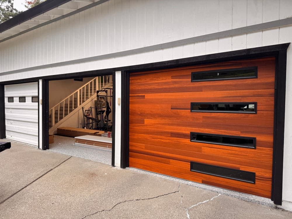 Modern wooden garage door with horizontal slats and windows, alongside a traditional white garage door.