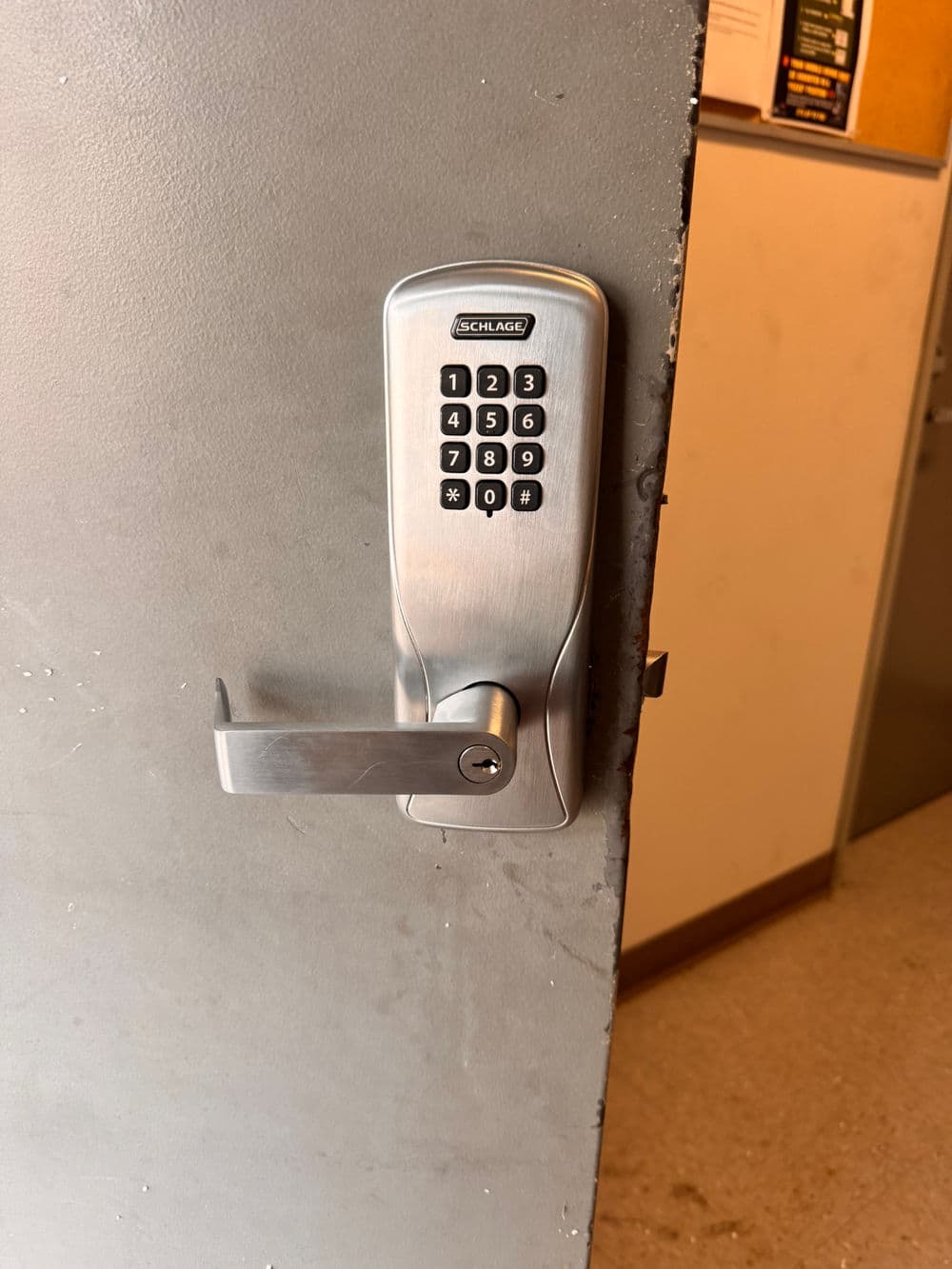Electronic keypad door lock on a gray door, featuring a lever handle and numeric keypad.